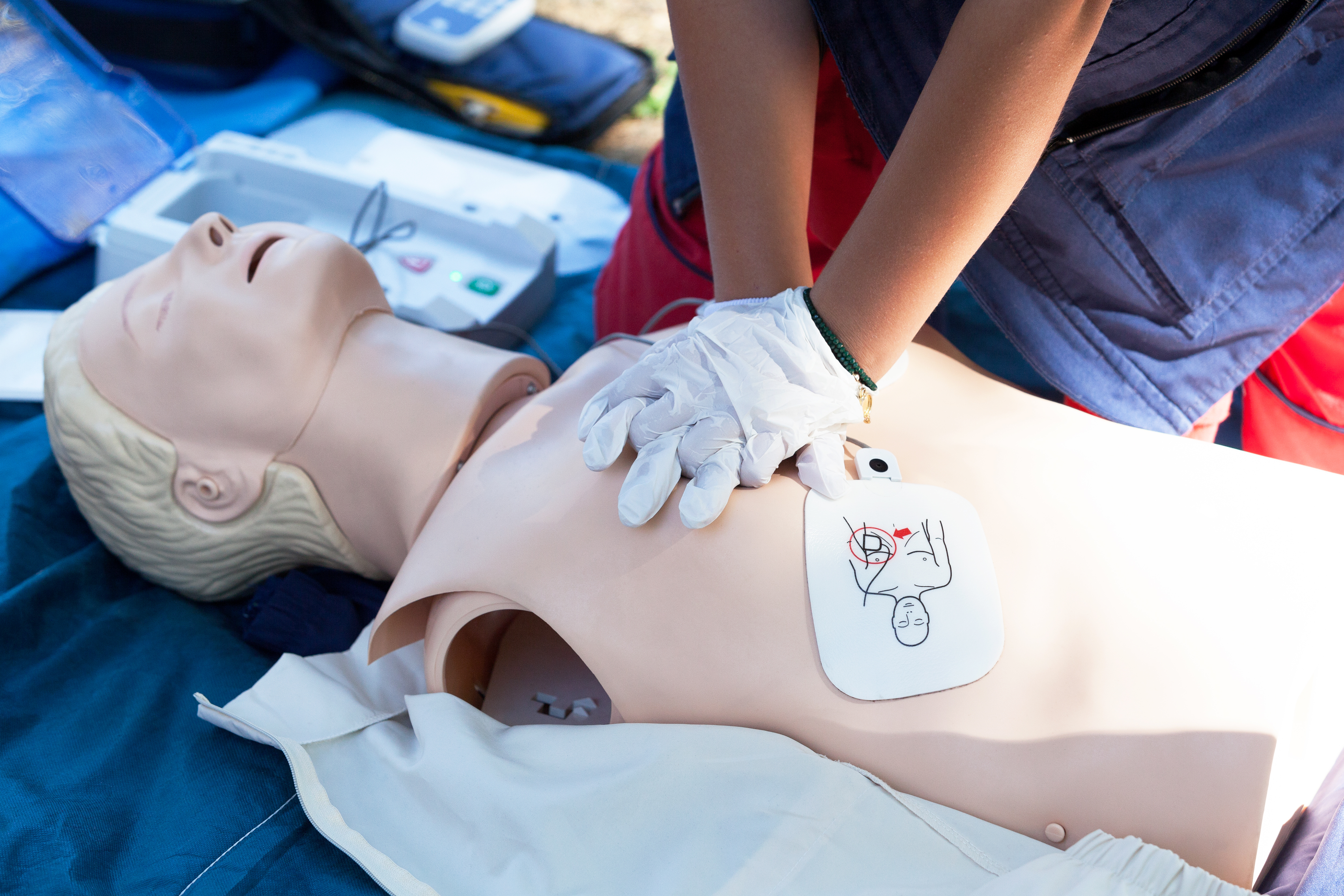 View of hands doing CPR with AED pads on CPR dummy.