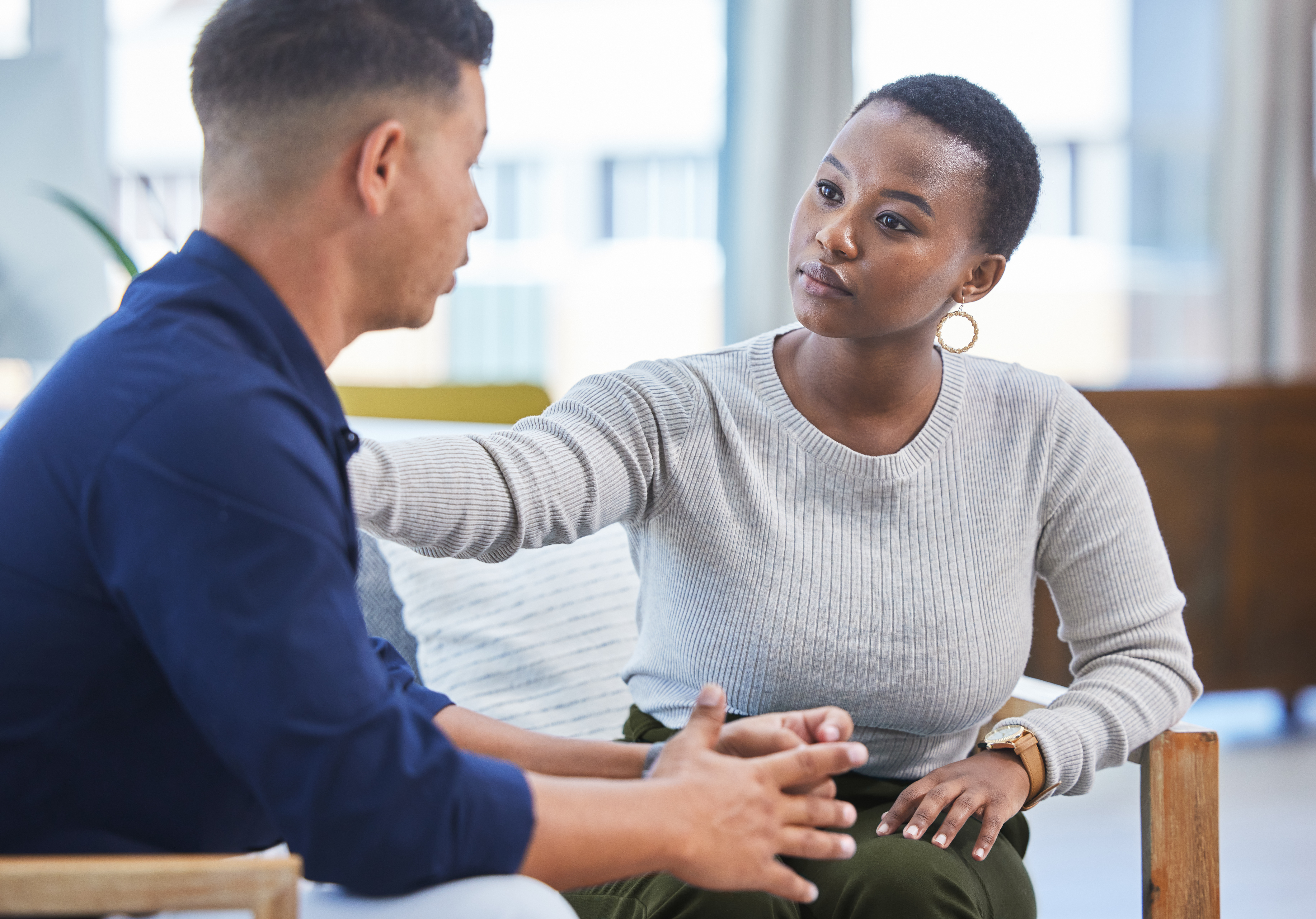 Woman and Man sitting down. Man is talking and woman is listening and offering support.