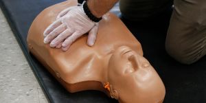 Gloved hands doing CPR on a mannequin.