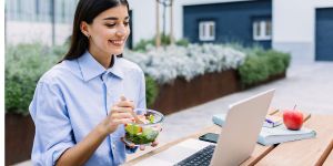 Woman outside at a table looking at her laptop while eating lunch.