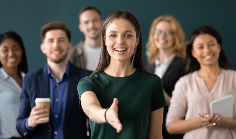 Woman reaching out to shake hands with group of people on background