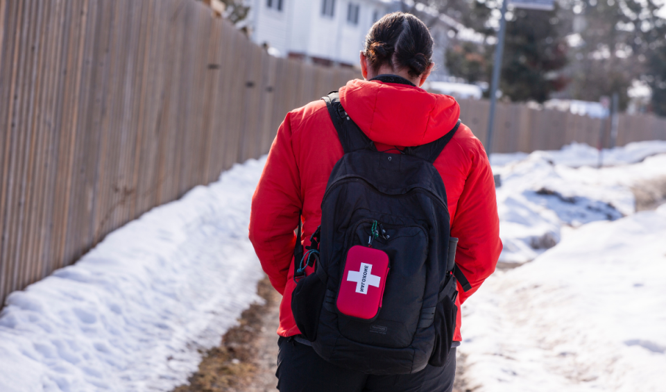 Person walking with Naloxone kit clipped to their backpack.