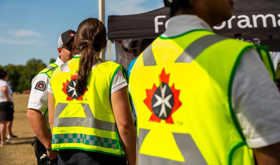 Close-up of St. John Ambulance volunteers wearing yellow safety vests with the organization's eight-pointed cross logo, walking through a festival crowd at Folklorama.