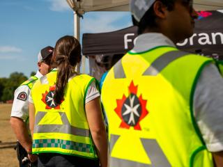 Close-up of St. John Ambulance volunteers wearing yellow safety vests with the organization's eight-pointed cross logo, walking through a festival crowd at Folklorama.