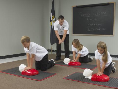 A group of children learning CPR from an SJA first aid instructor.